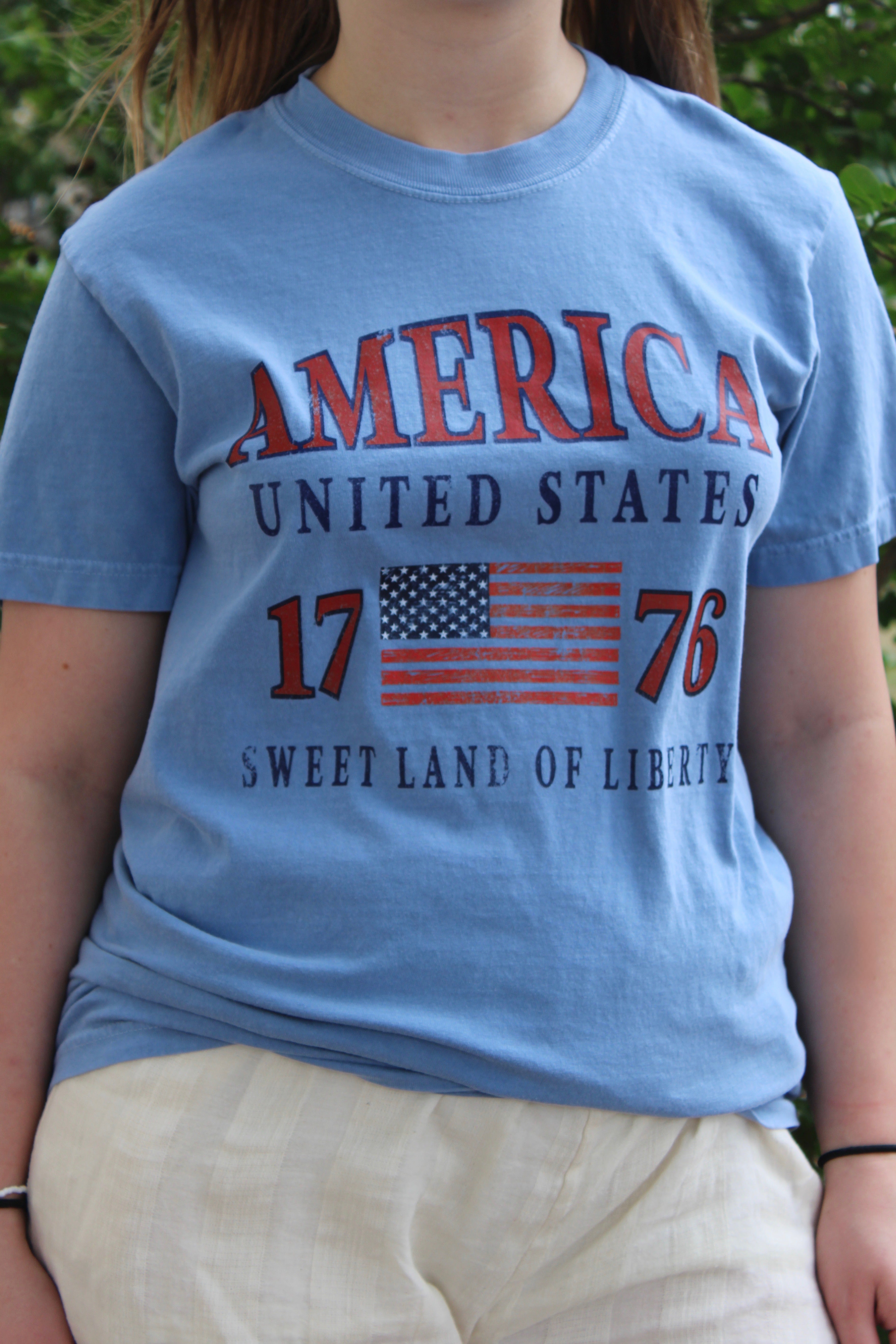 Blue t-shirt with 'America United States 1776 Sweet Land of Liberty' text and American flag design.